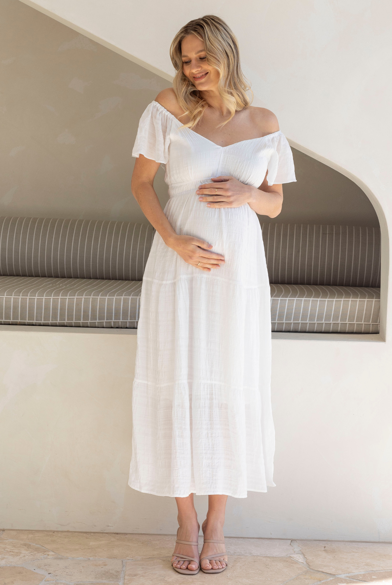 Pregnant woman in a white dress standing in a modern interior setting.