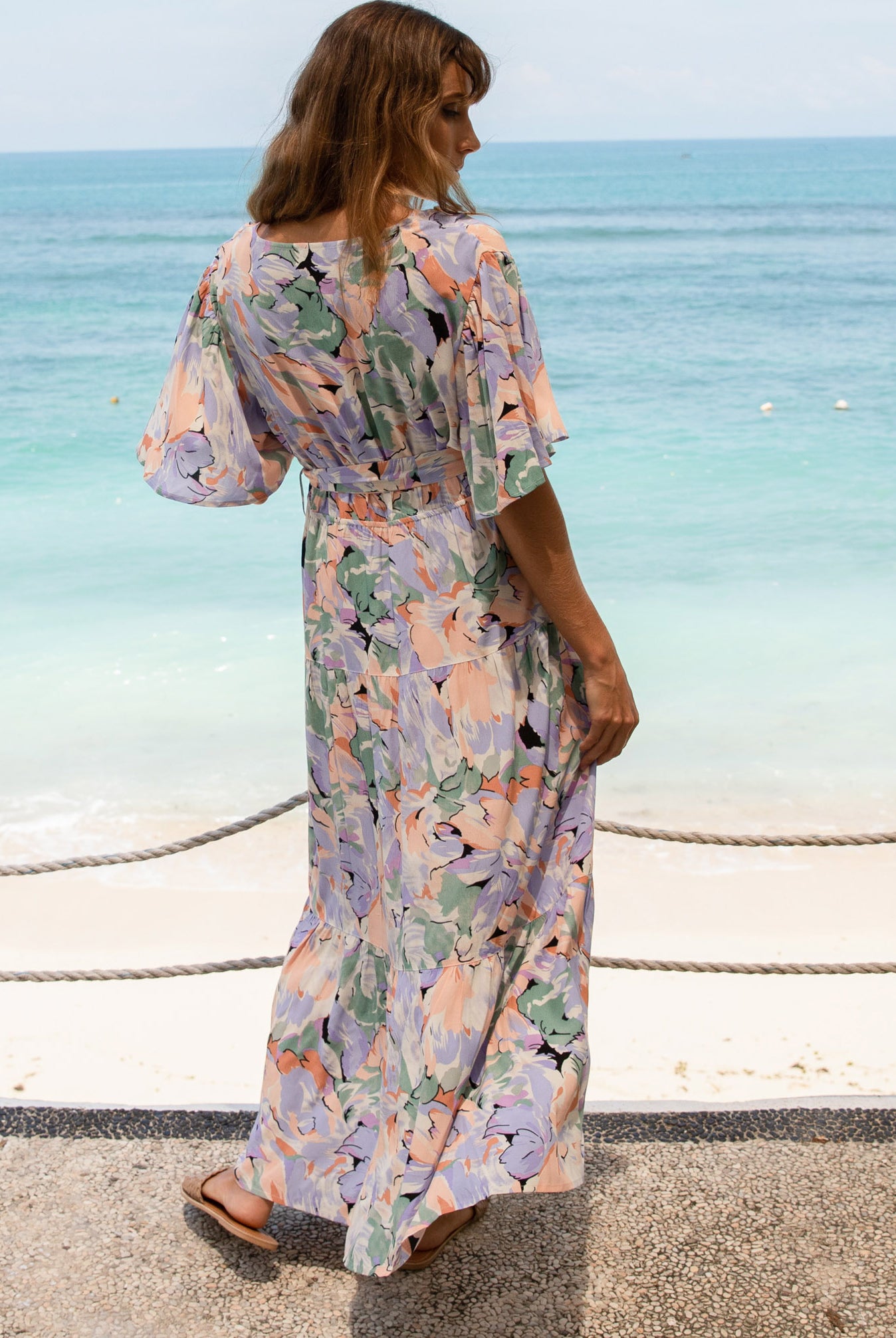 A woman in floral lavender maternity baby shower dress standing on the beach (6672554033246)