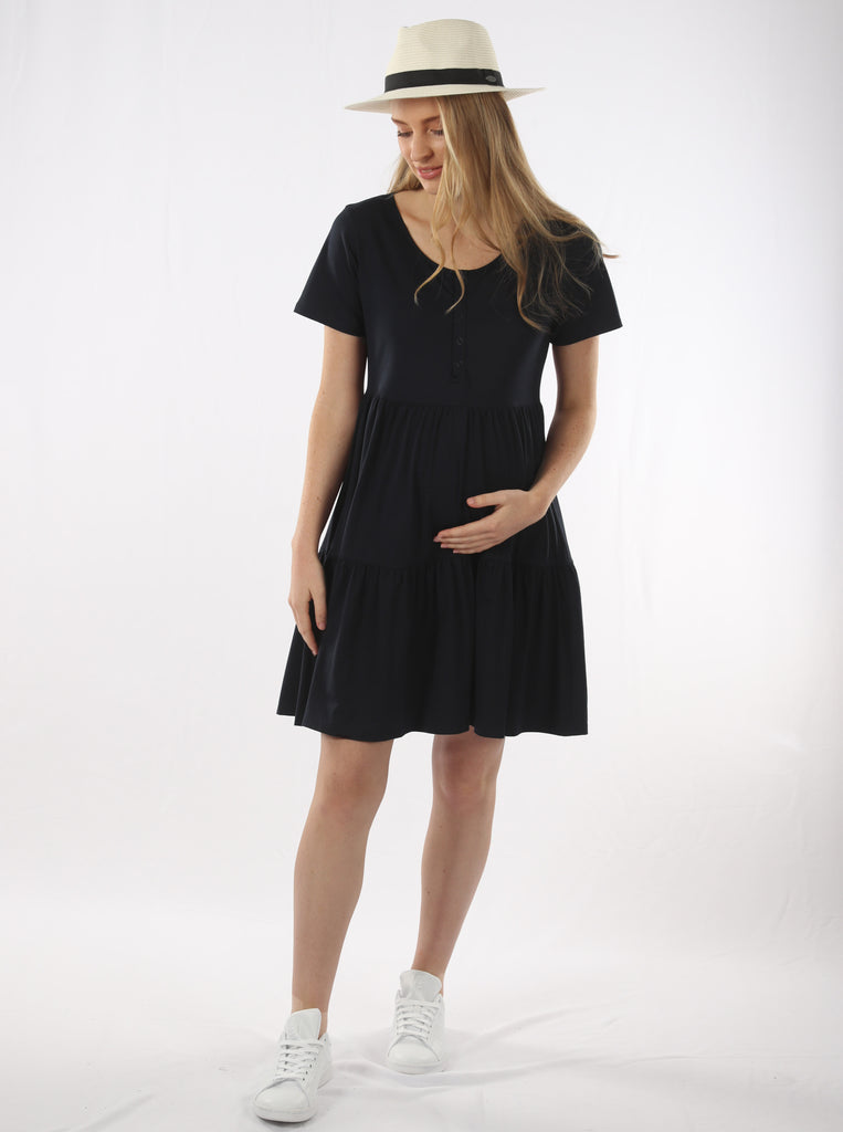  A young pregnant woman in Short Sleeve Tiered Mini Black Maternity  Dress & hat looking down smiling (4827569684574)
