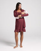 Woman wearing a burgundy nightgown holding a baby against a white background