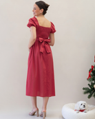 Woman in a red dress with a bow standing next to a small white dog on a white background