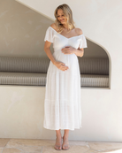 Pregnant woman in a white dress standing in a modern interior setting.