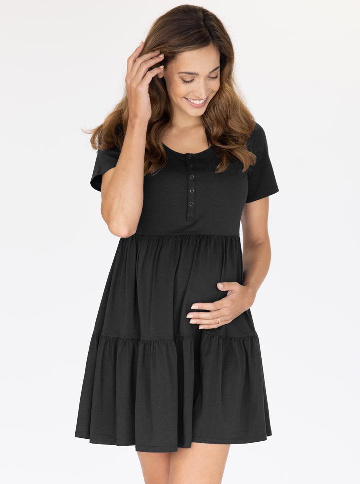 Front view -  A young pregnant woman in Short Sleeve Tiered Mini Black Maternity  Dress touching her bump & smiling. (4827569684574)