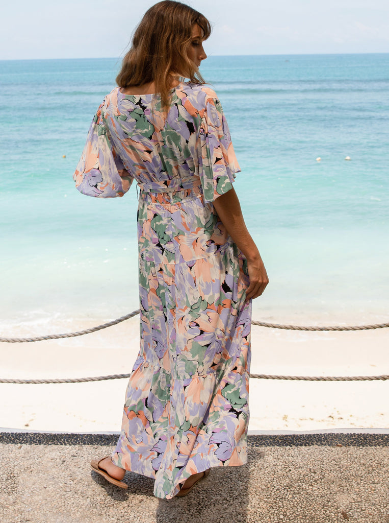 A woman in floral lavender maternity baby shower dress standing on the beach (6672554033246)